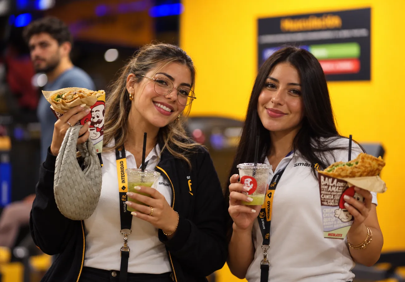 Dos personas del equipo de Smart Fit sonriendo con crepas y bebidas NICOLATI'S